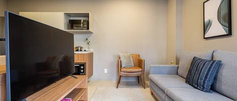 Uma sala de estar moderna com televisão de tela plana, um sofá cinza, uma mesa de centro de madeira e uma pequena mesa lateral.
