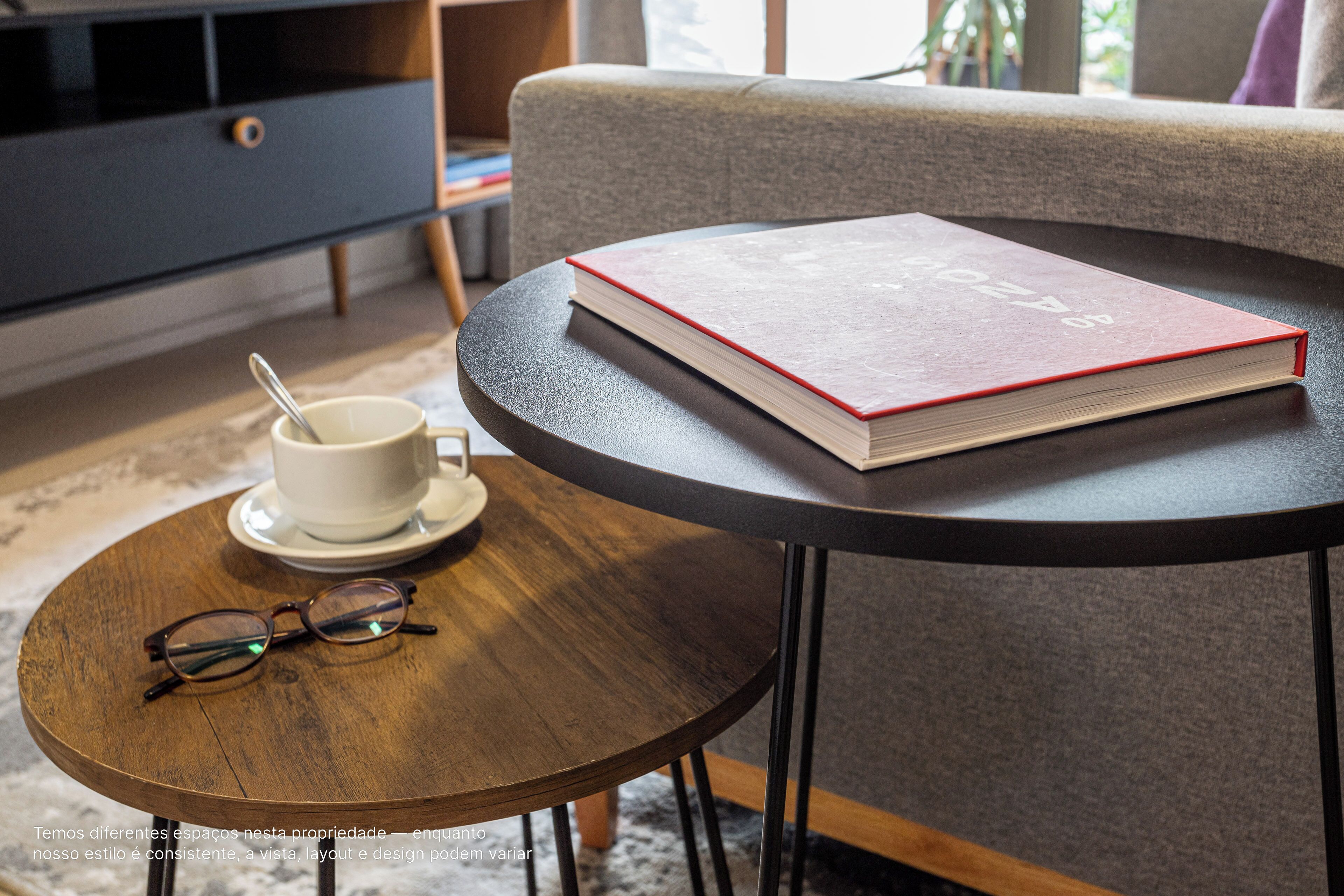 A round wooden table with a book, a pair of glasses, and a cup with a spoon on a saucer.