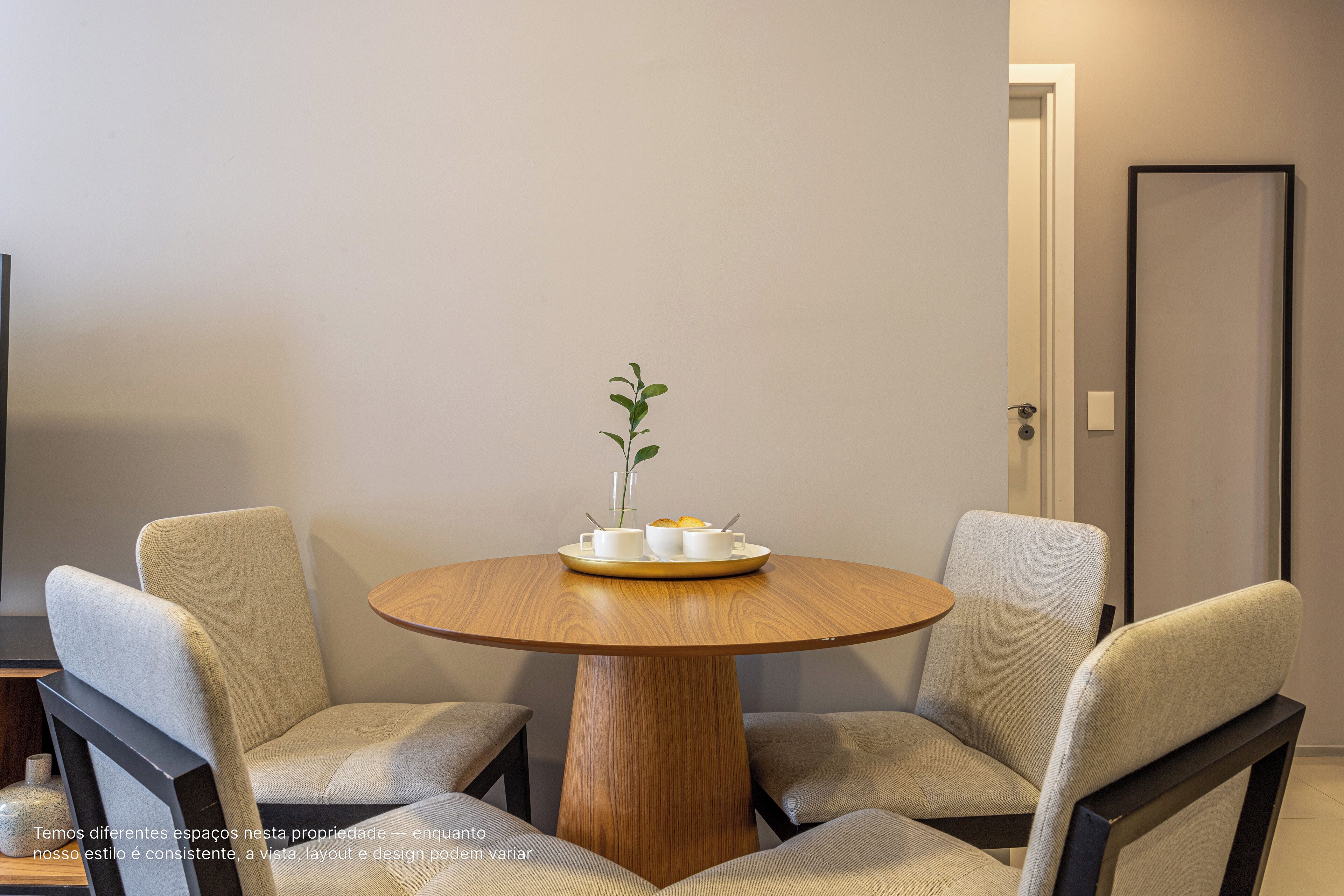 A round wooden table with four chairs, a small potted plant, and a tray with cups and a bowl.