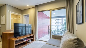 Ein modernes Wohnzimmer mit einem Flachbildfernseher auf einem Holzbodenständer, einer Couch und einer Glasschiebetür, die zu einem Außenbalkon führt.