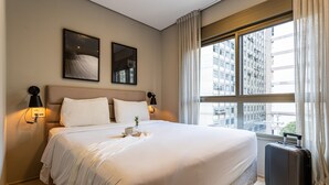 Ein Hotelzimmer mit einem großen Bett, zwei Wandlampen und einem Fenster mit Vorhängen.