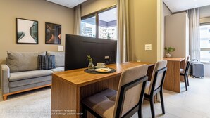Ein modernes Hotelzimmer mit einer Sitzecke, einem Holztisch und Blick auf die Stadt.