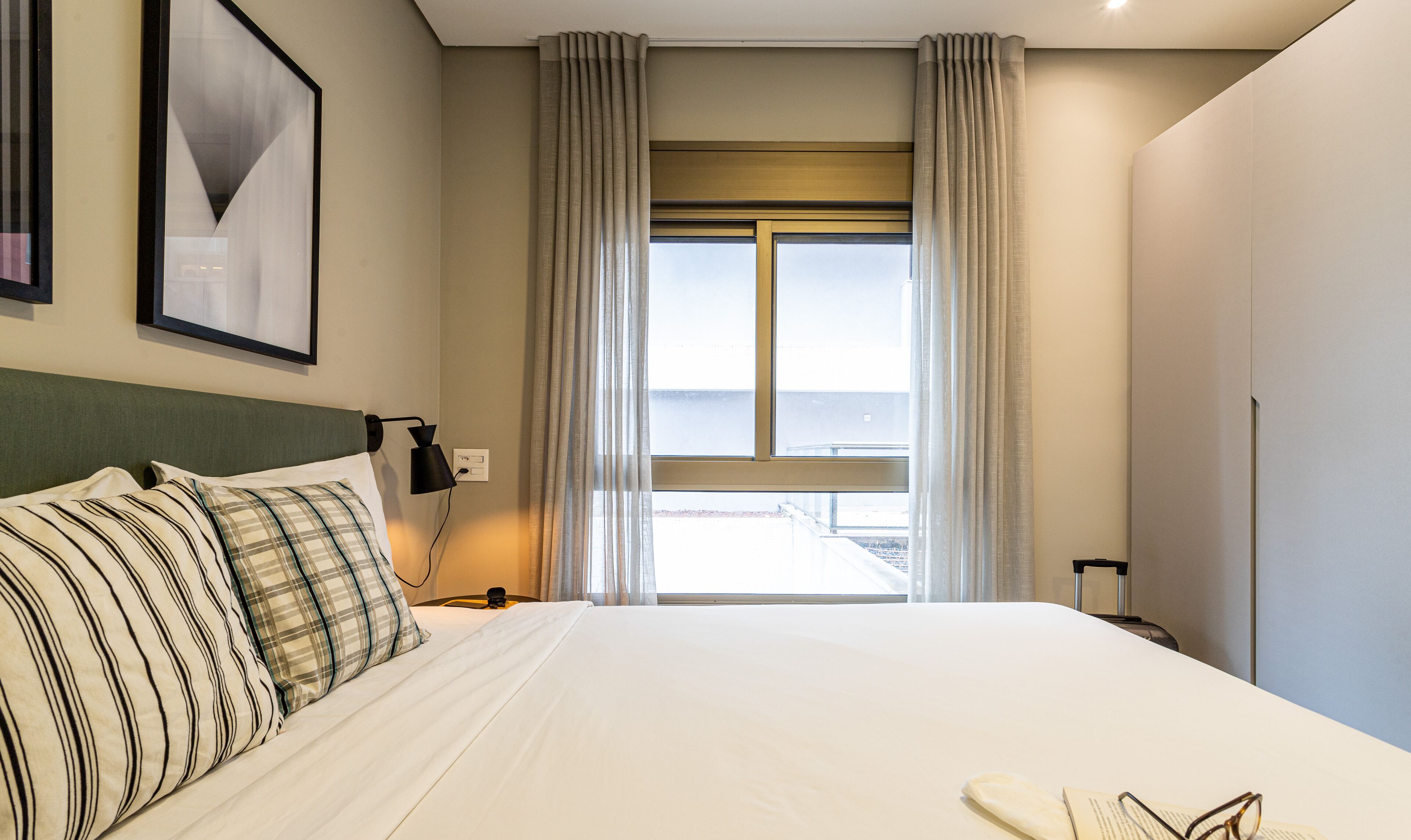 A hotel room with a large bed, a nightstand, a lamp, a window with curtains, and a framed picture on the wall.