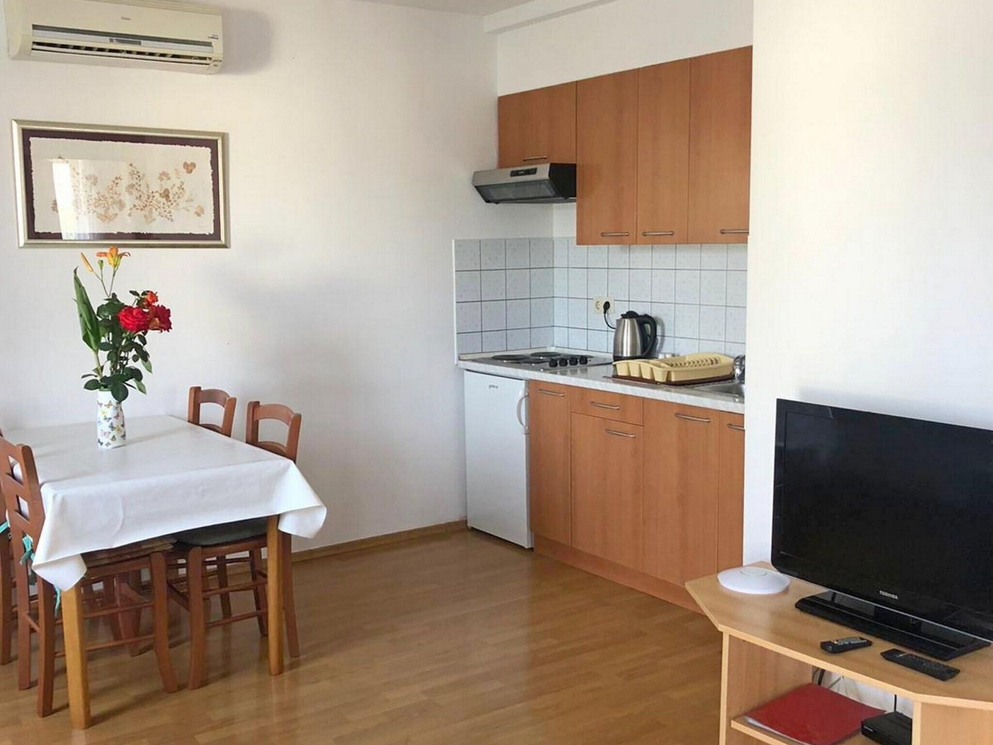 A compact kitchen with wooden cabinets, a tiled backsplash, a small stove, and a dining area with a table and chairs.