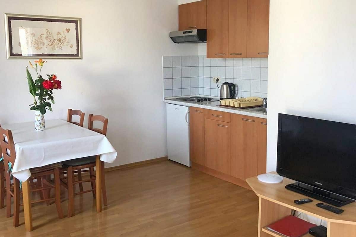 A compact kitchen with wooden cabinets, a tiled backsplash, a small stove, and a dining area with a table and chairs.