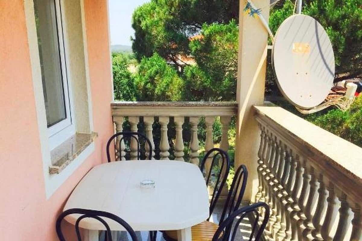 A balcony with a table and chairs, overlooking a garden with trees and a distant view.