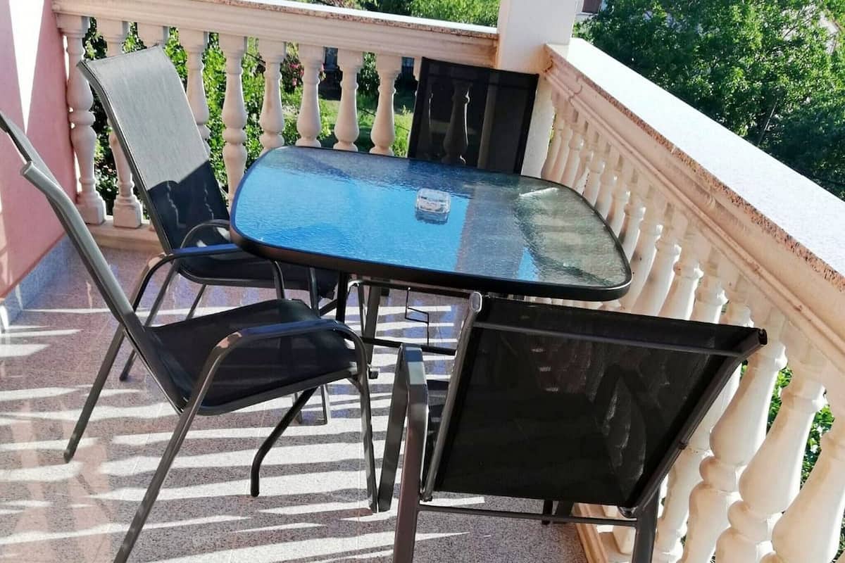 A small outdoor balcony with a glass table and two chairs.