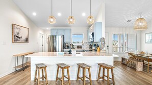 Une cuisine moderne dotée d’un îlot central, de tabourets de bar, de luminaires suspendus et offrant une vue sur l’espace repas.