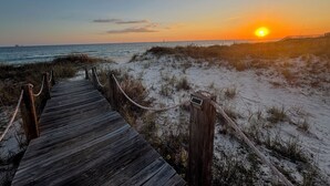 Une promenade en bois menant à une plage bordée de dunes de sable, avec un coucher de soleil en arrière-plan.