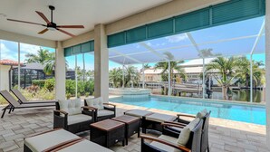 Ein Poolbereich mit Liegestühlen und Tischen, einem Deckenventilator und Blick auf Pool und umliegende Landschaft.