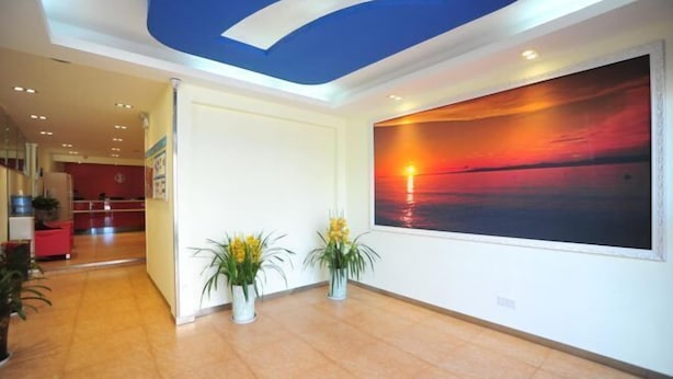 Eine Hotelhalle mit einem großen Sonnenuntergangsgemälde, einem Empfangstresen und Topfpflanzen.