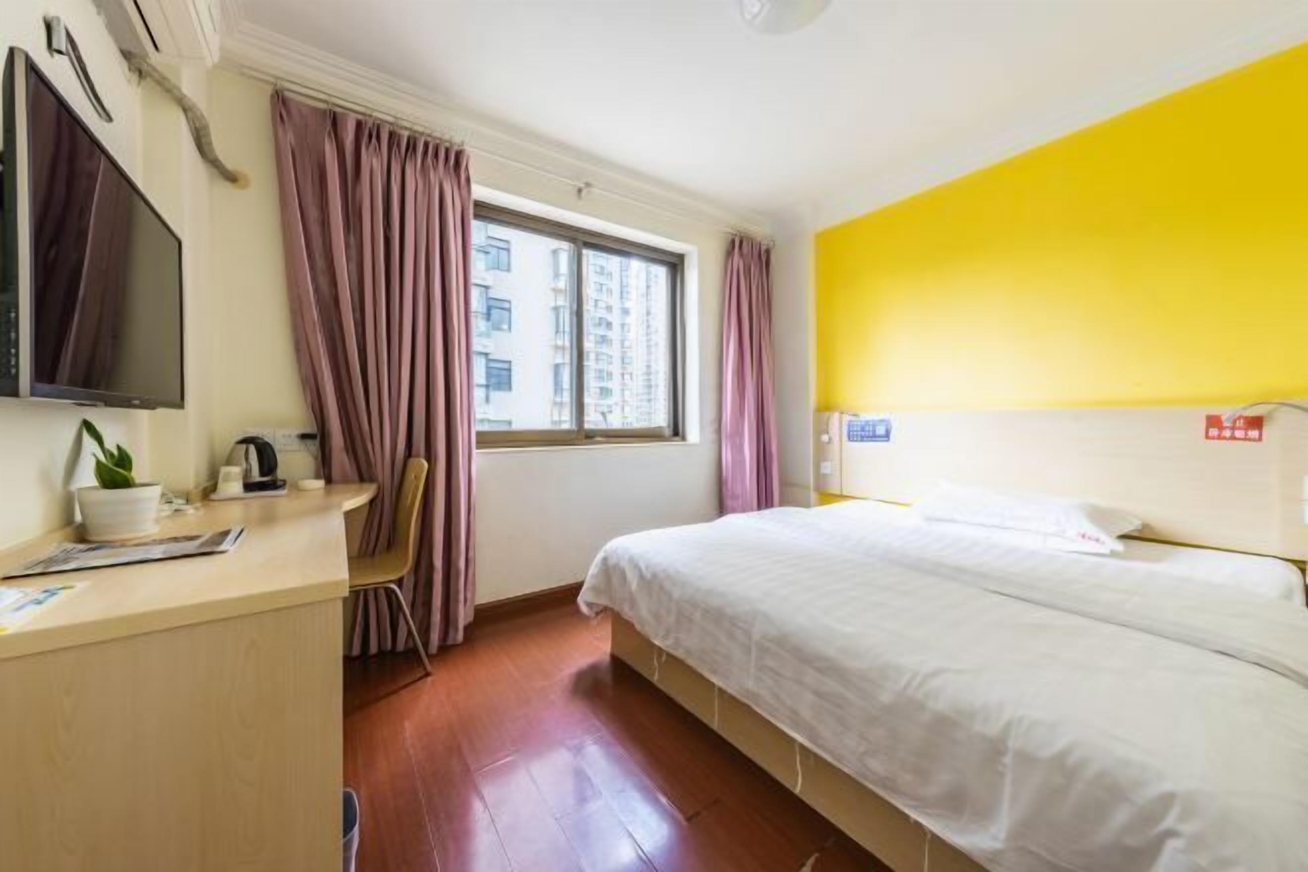 A hotel room with a bed, a desk with a computer, a TV, and a window with curtains.