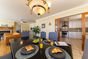 Un coin repas avec une table mise pour le petit-déjeuner, comprenant des croissants et du jus d’orange, et donnant sur la cuisine.