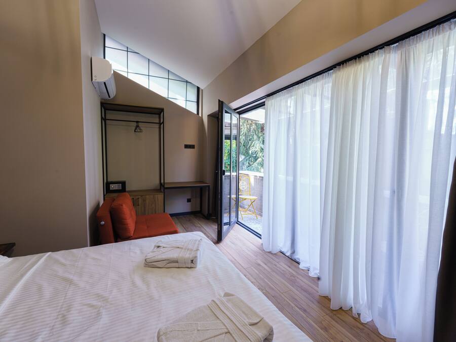 A hotel room with a bed, a chair, a table, and a sliding glass door to the outside.