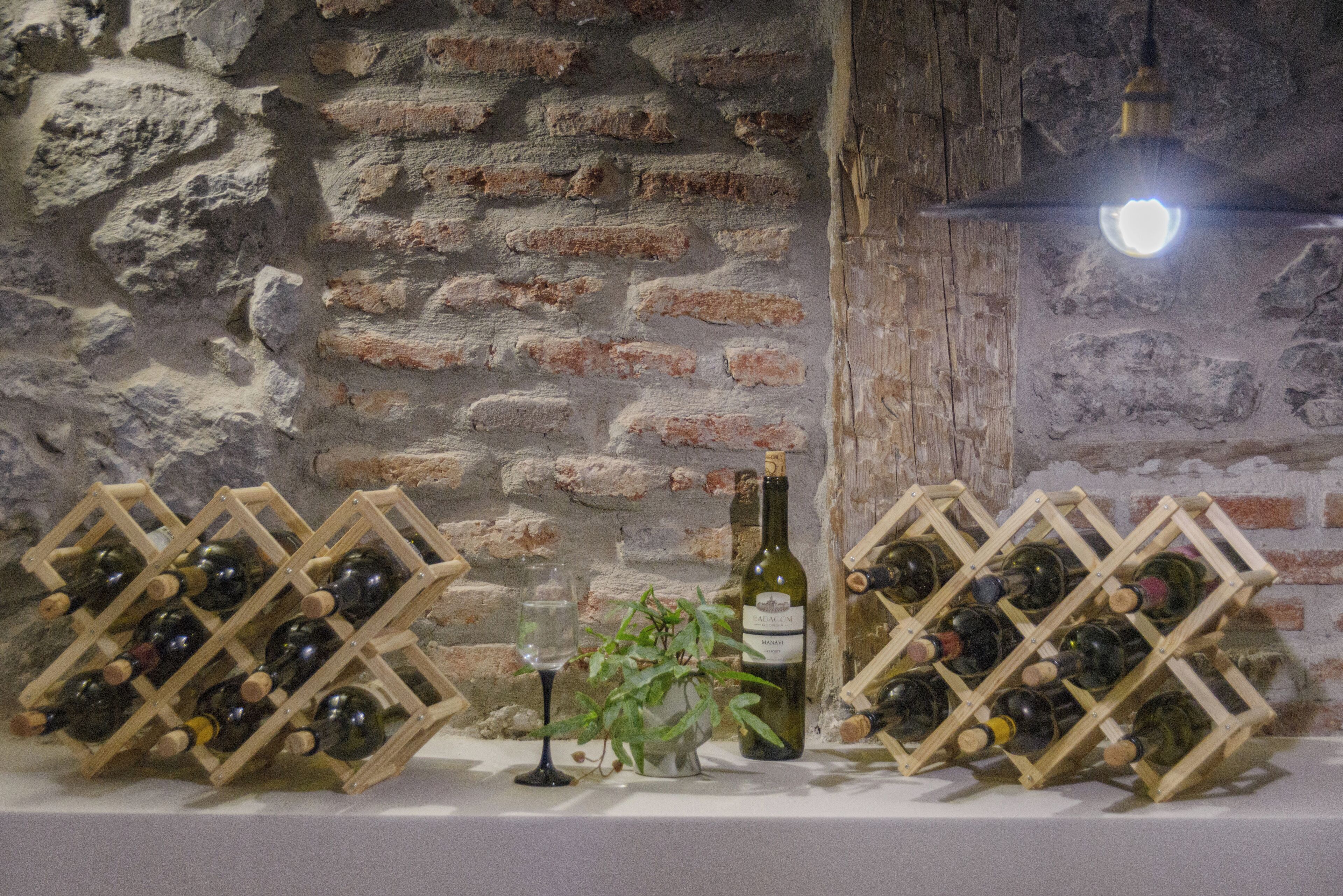 Una botellera con botellas y copas frente a una pared de piedra.