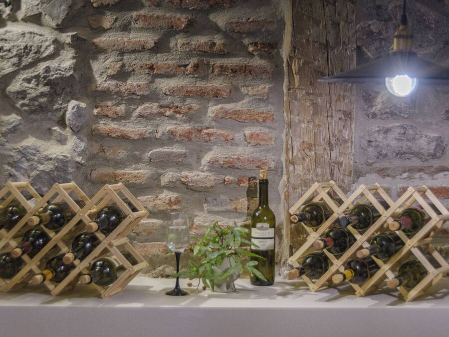 Una botellera con botellas y copas frente a una pared de piedra.