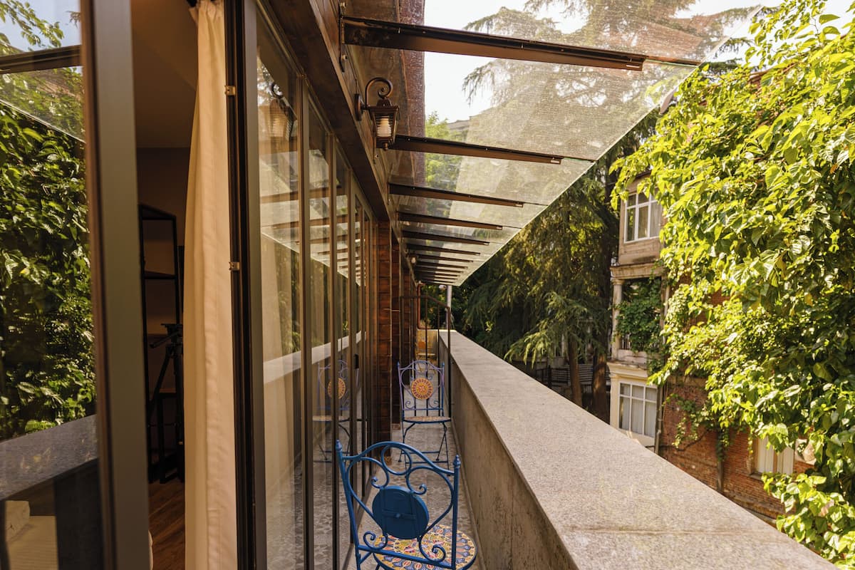 Un balcón estrecho con piso estampado, una silla de metal y un ventanal de vidrio que da a una habitación.