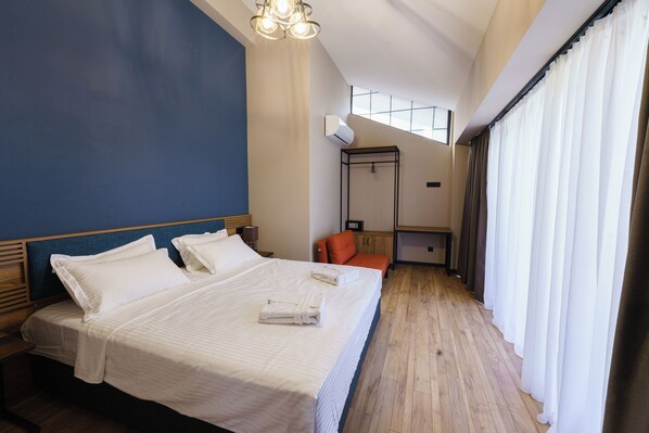 A hotel room with a large bed, a wooden floor, a desk with a chair, and a window with curtains. - ARAKI Sololaki (Tbilisi)