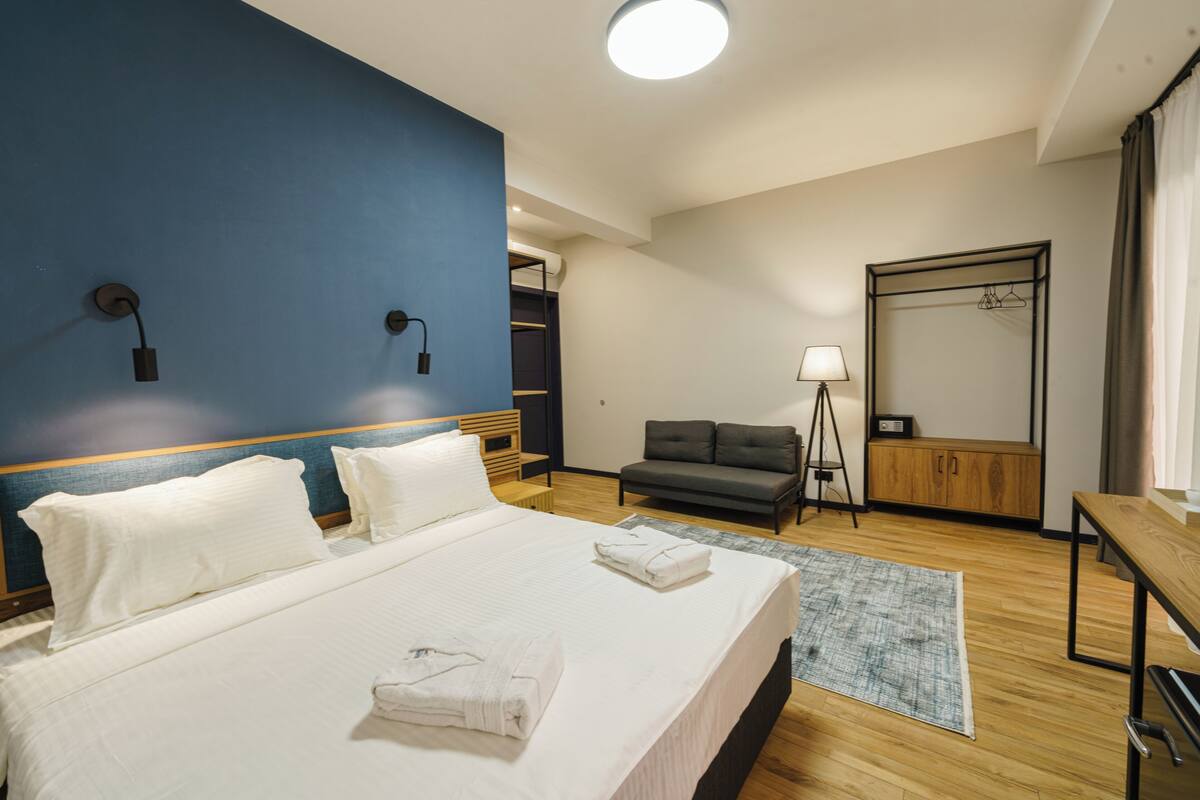 Una habitación de hotel con una cama grande, una mesita de noche, una lámpara, un espejo y un armario.