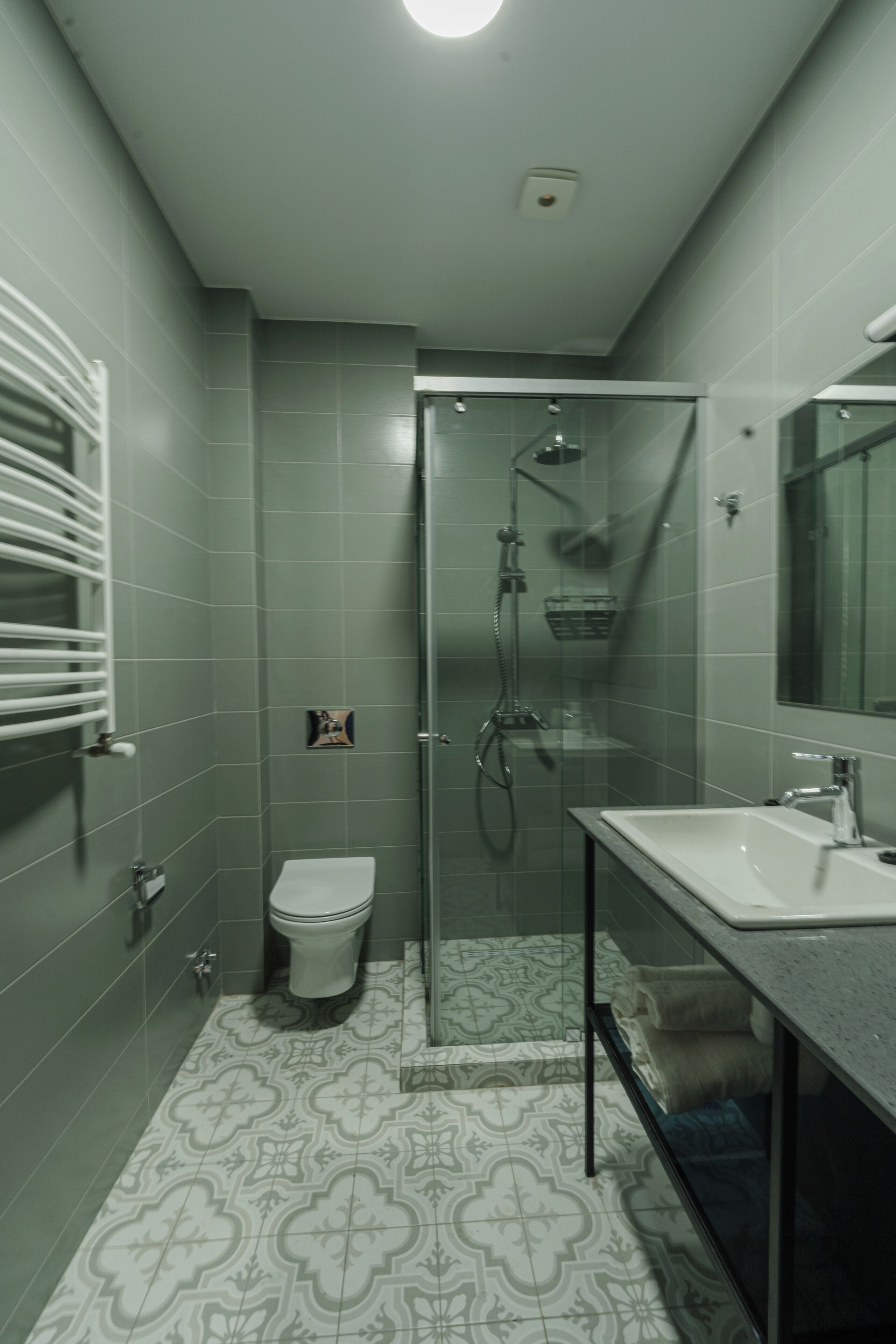 A modern bathroom with a glass shower enclosure, a white sink, and patterned floor tiles.