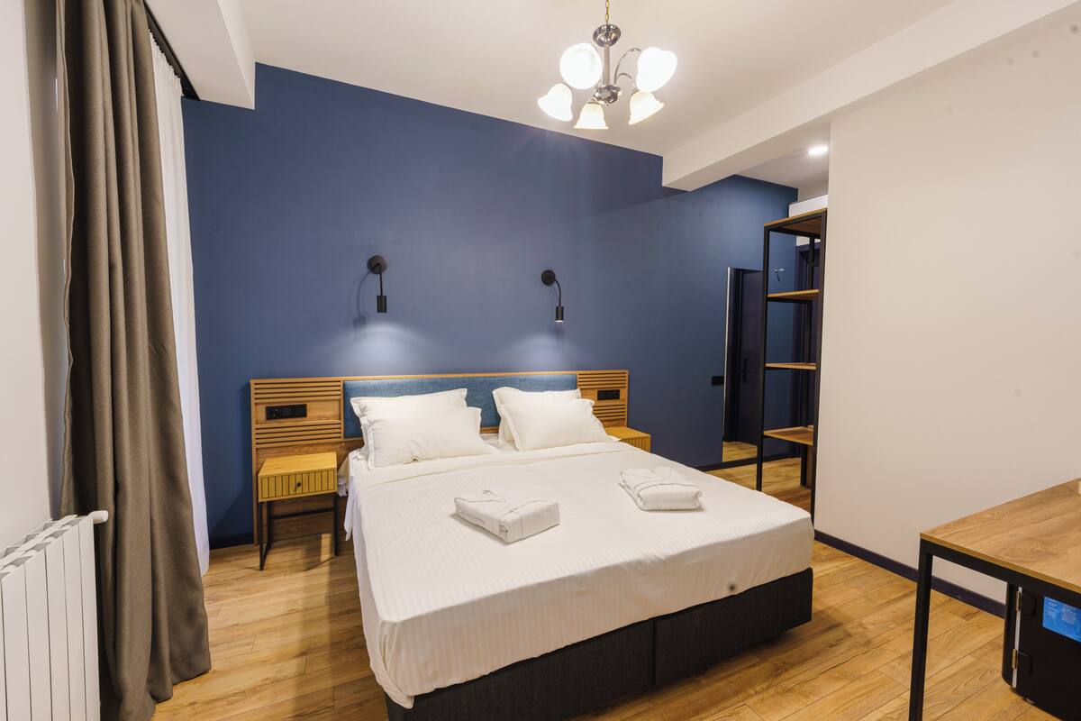 Una habitación de hotel moderna con una cama grande, cabecera de madera, dos mesitas de noche, un escritorio y un armario.