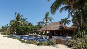 Un complexe hôtelier doté d’une piscine, d’une plage et de bâtiments à toits de chaume.