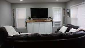 A living room with a black leather sofa, a flat-screen TV mounted on the wall, and a wooden countertop above a white cabinet. - Charming 4-bedroom house with WiFi and AC in fantastic Hawley (Hawley)