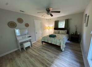 Een slaapkamer met een bed, een bureau, een plafondventilator en een nachtkastje.