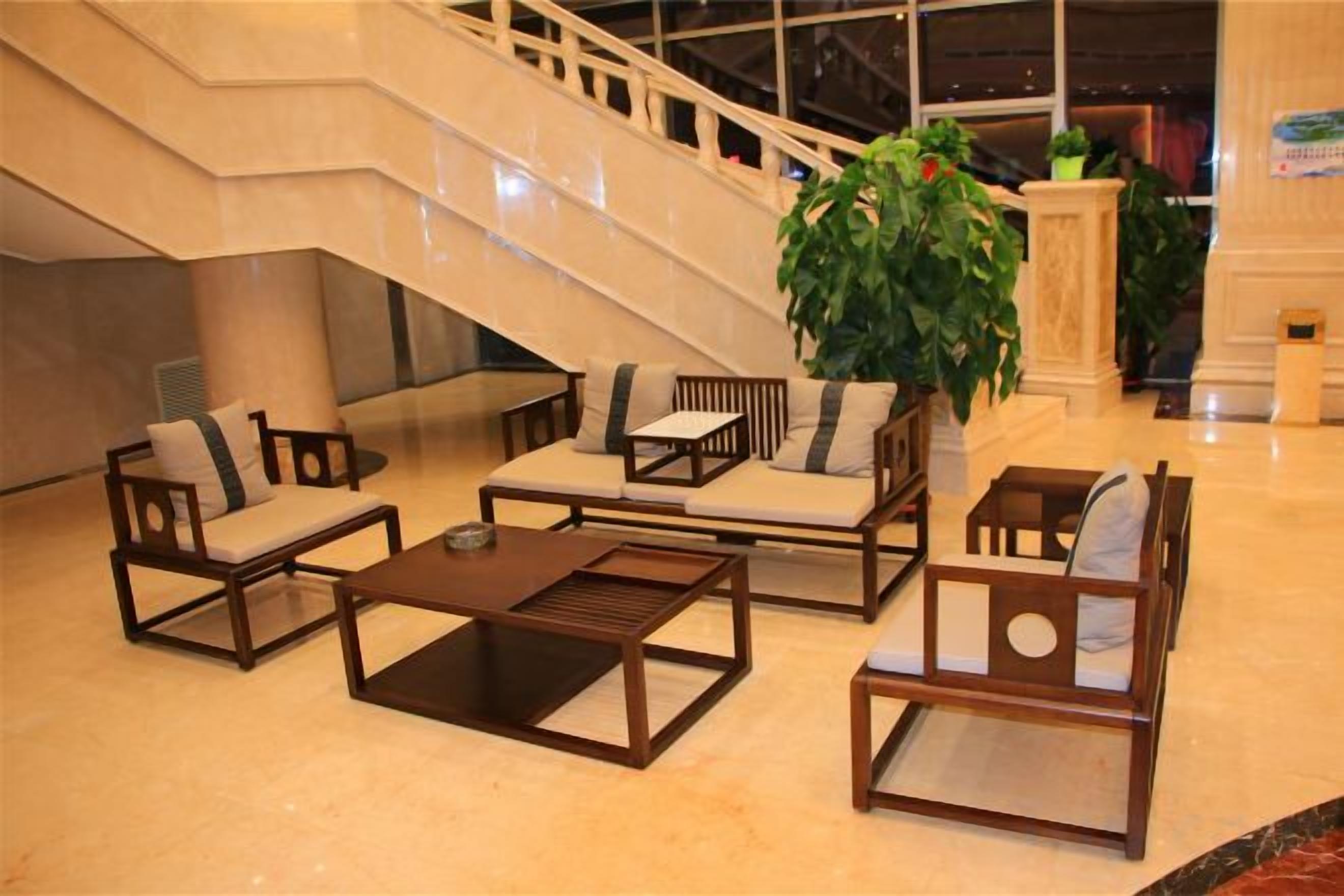 Un hall d’entrée avec un escalier, un espace détente avec des canapés et des fauteuils, et une grande plante en pot.