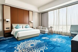 Habitación de hotel con una cama grande, un sofá, una silla, una mesita y vistas al exterior.