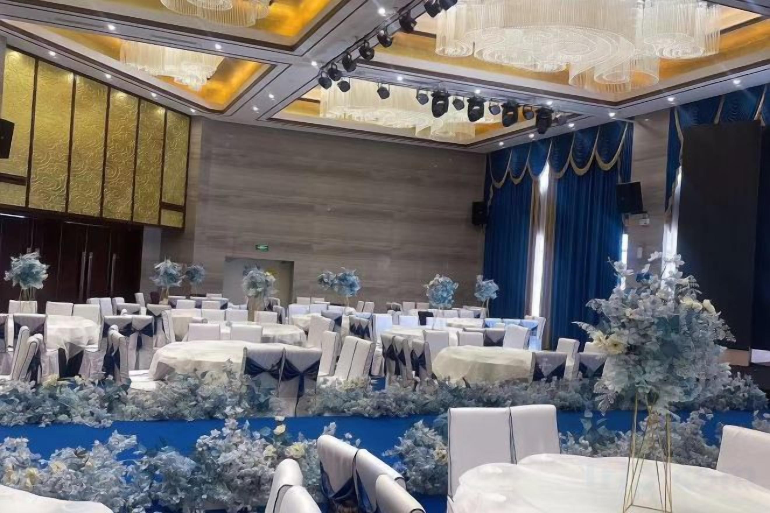 Een feestzaal met ronde tafels, stoelen en bloemdecoraties.