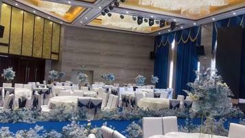 Een feestzaal met ronde tafels, stoelen en bloemdecoraties.