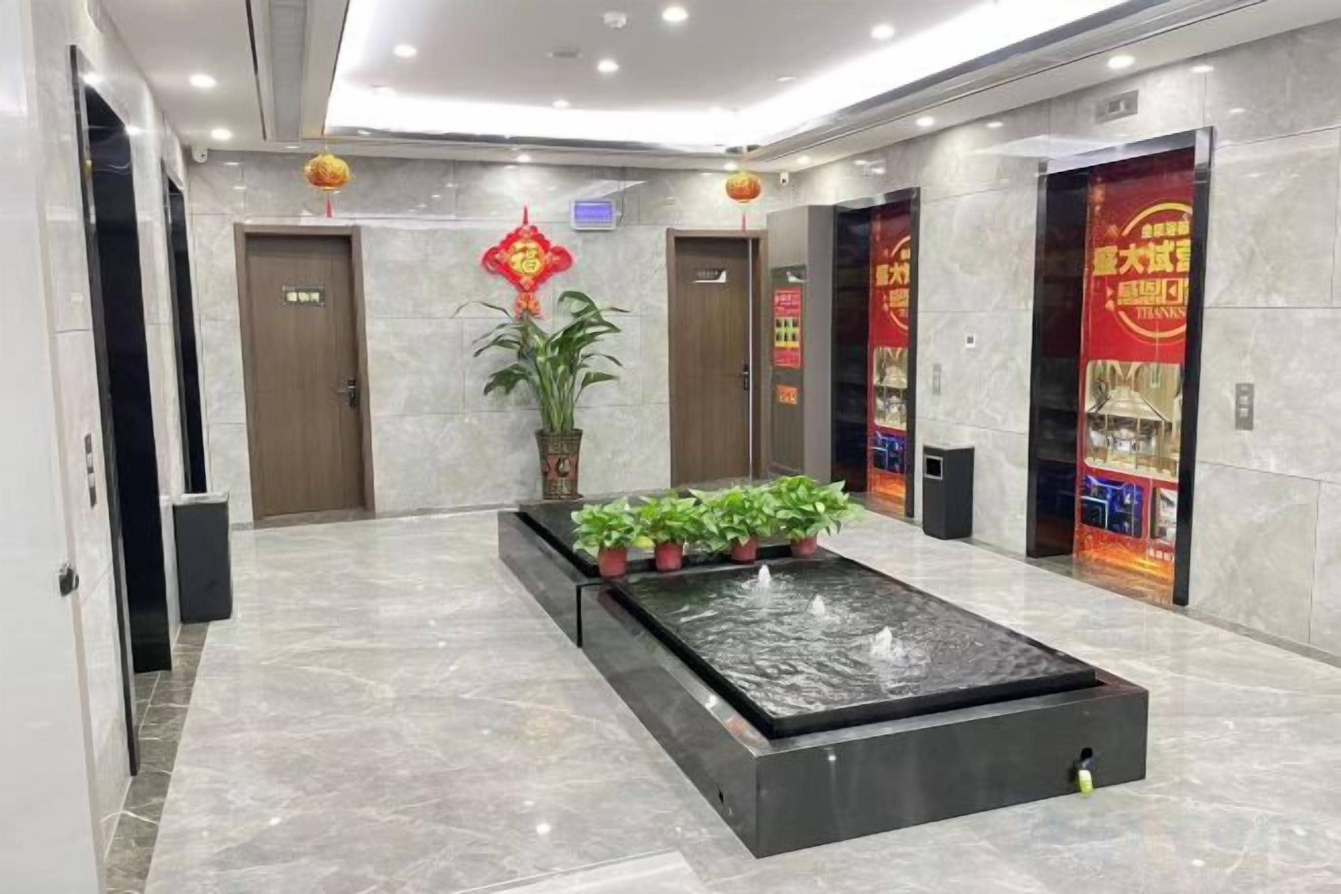 A lobby with a water feature, potted plants, and red decorations.