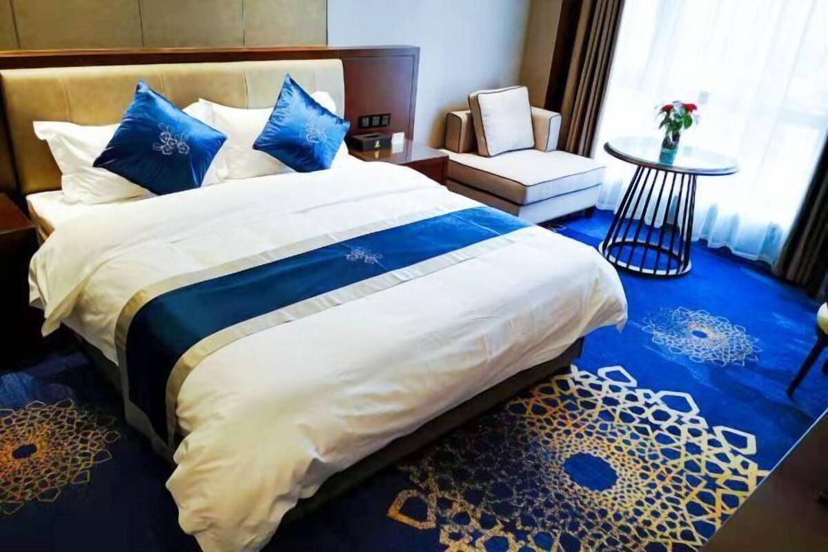 A hotel room with a large bed, a sofa, a small table with a vase, and a patterned carpet.