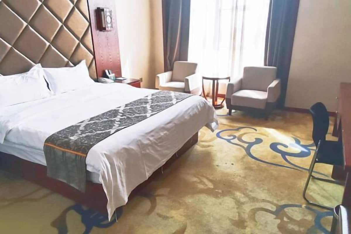 A hotel room with a large bed, two armchairs, a small table, and a patterned carpet.