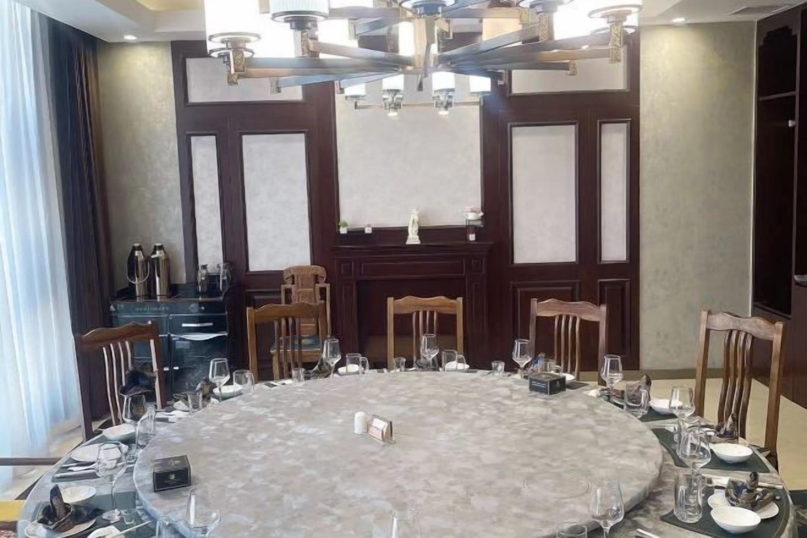 A round dining table set for a meal with chairs, a chandelier, and a fireplace in the background.