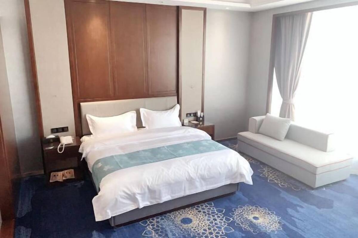 A hotel room with a large bed, a sofa, a nightstand, a lamp, and a window with curtains.