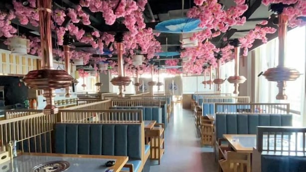 A restaurant with booths and tables, featuring hanging pink flowers and copper pendant lights. - Shizuishan Jinguan Hotel (Shizuishan)