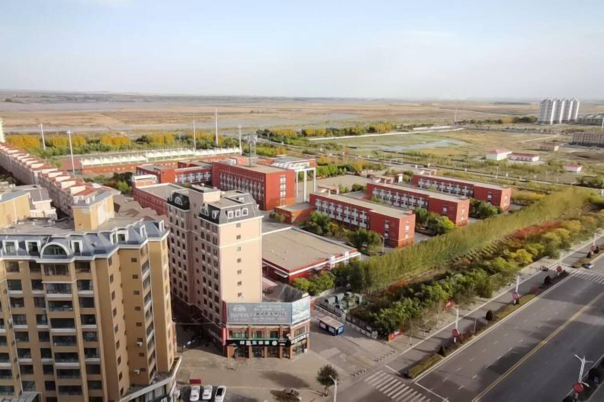 Un edificio de varios pisos con una fachada destacada en rojo y beige, rodeado de un área ajardinada con árboles y una calle.