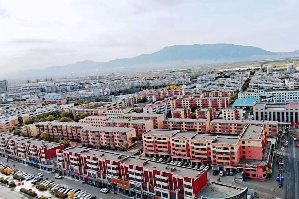 Un paisaje urbano con edificios de varios pisos, un estacionamiento y montañas al fondo.