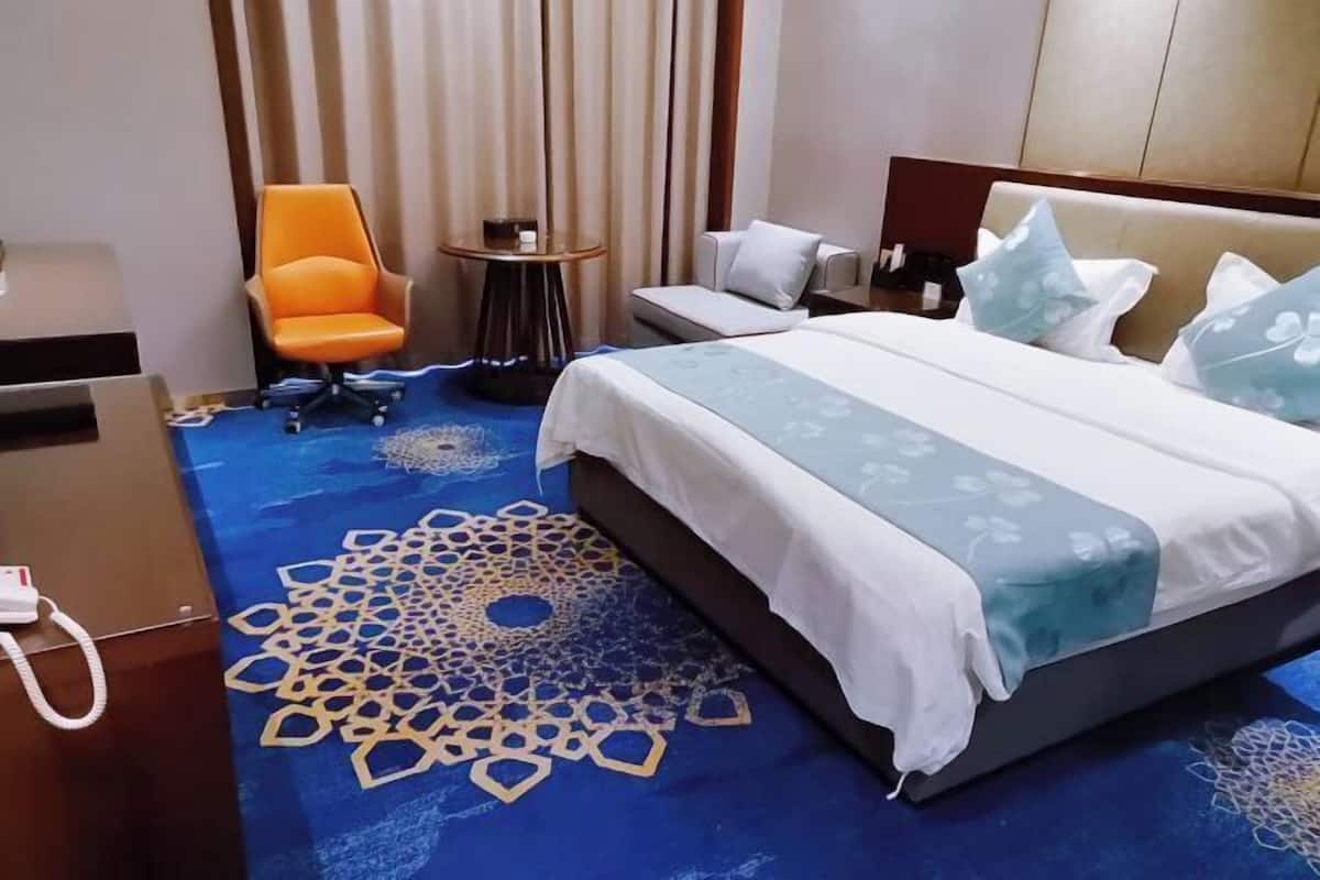 A hotel room with a large bed, a sofa, an orange chair, a small table, and a patterned carpet.