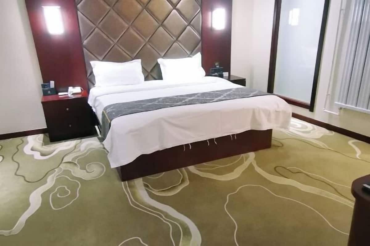 A hotel room with a large bed, a headboard, a nightstand, and a carpet with a wavy pattern.