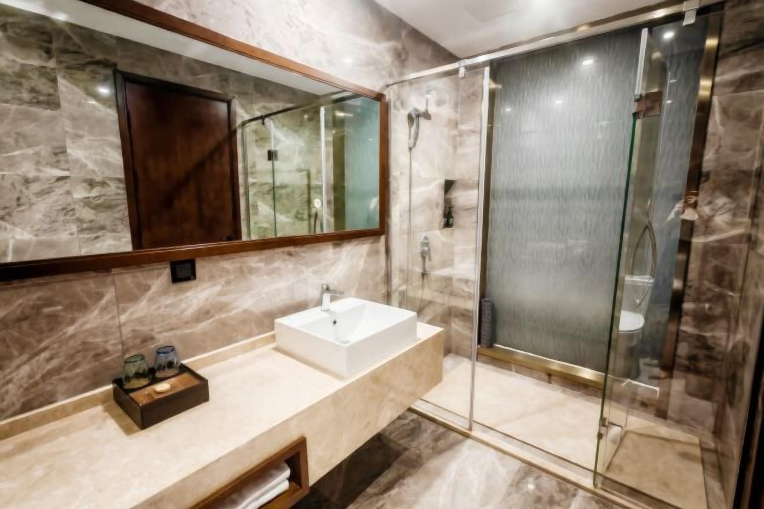 A modern bathroom with a marble vanity, a glass shower enclosure, and a large mirror.