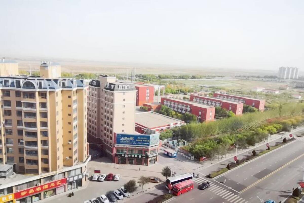 Un edificio de varios pisos con una planta baja comercial, un estacionamiento y un autobús rojo en la calle.