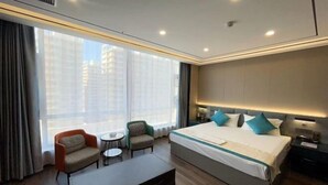 A hotel room with a large bed, two armchairs, a small table, and a nightstand. - Shizuishan Jinguan Hotel (Shizuishan)