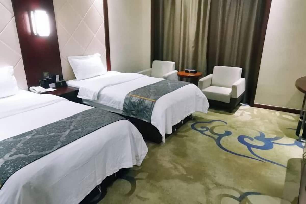 A hotel room with two beds, a small table, a chair, and a carpeted floor.
