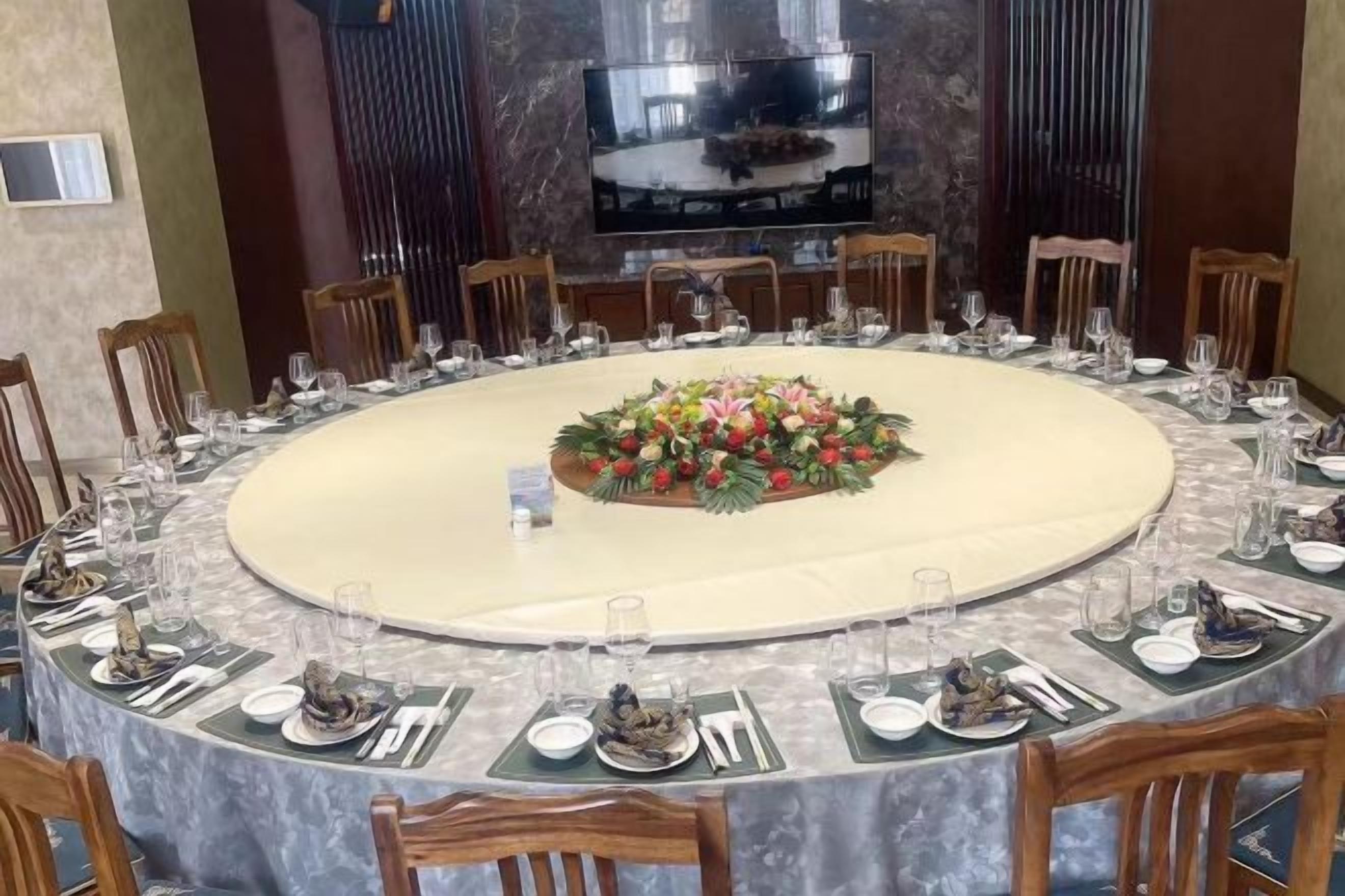 Una mesa de comedor redonda con un centro de mesa floral, rodeada de sillas y dispuesta con platos, vasos y cubiertos.