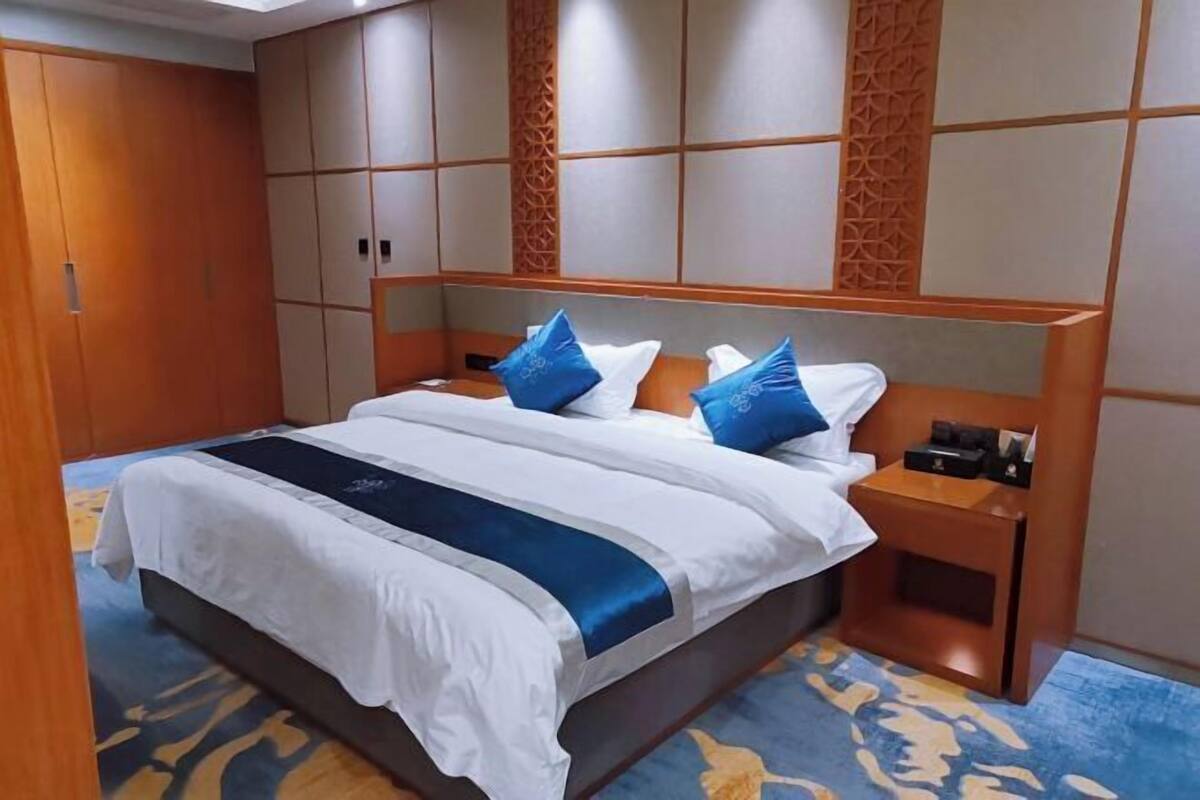 A hotel room with a large bed, a wooden wardrobe, and a nightstand with a lamp.