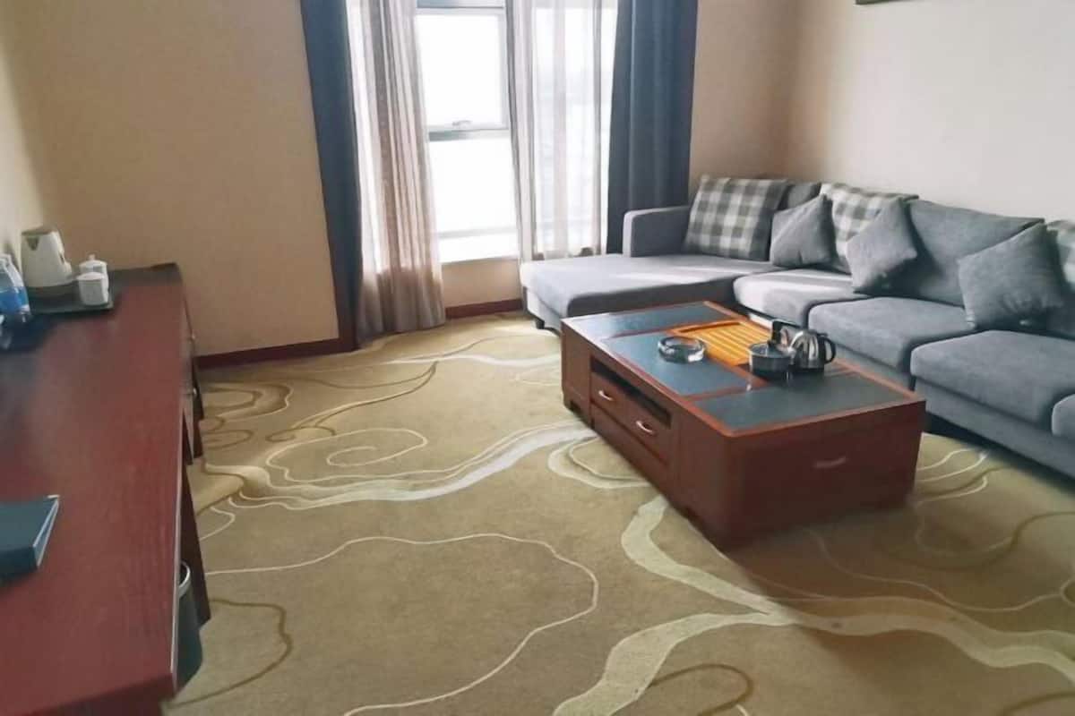 A living room with a sofa, a coffee table, a wooden side table, and a patterned carpet.