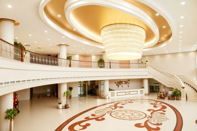 A spacious lobby with a grand chandelier, multiple staircases, and a decorative floor pattern.